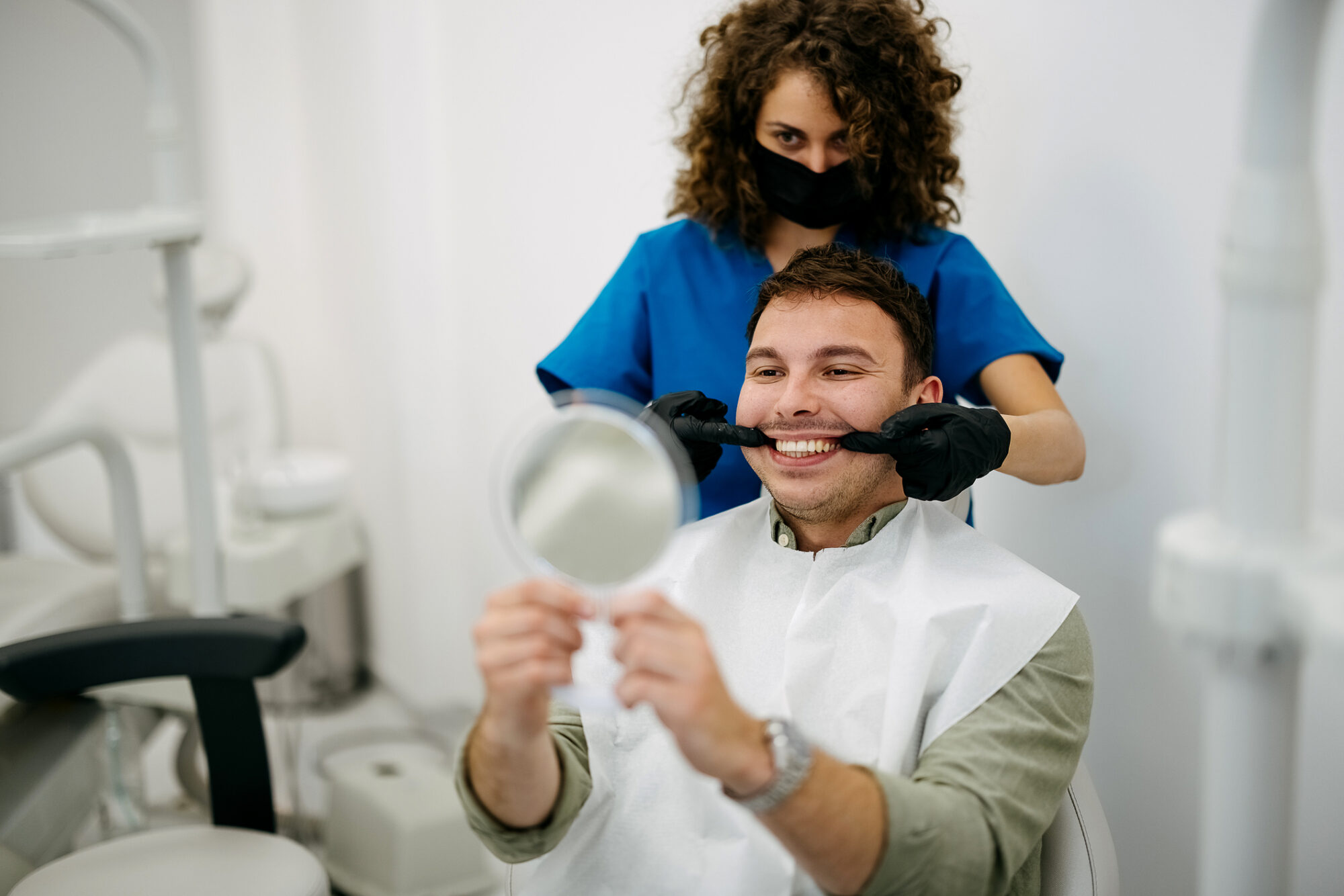 Male patient smiling in the mirror after getting dental bridges at Dream Smiles Dental